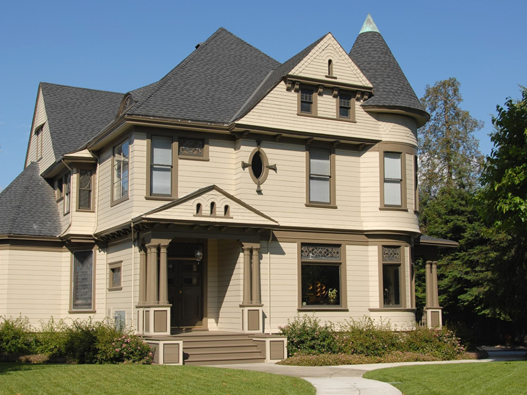 Victorian-style house with beige siding and dark trim, showcasing expert exterior painting by J.A. Painting & Decorations, surrounded by well-maintained landscaping.