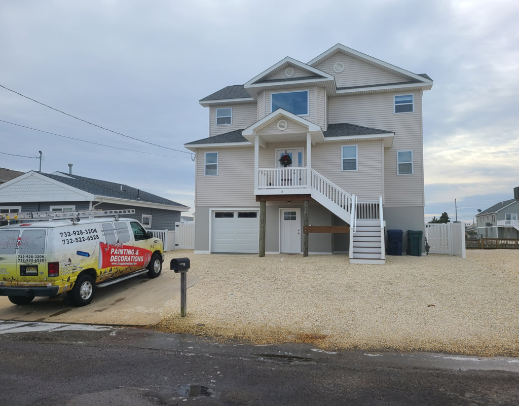 Residential property exterior with a beige house featuring multiple windows, a covered porch, and white railings, alongside a J.A. Painting & Decorations service van parked in the driveway, showcasing the company's branding and contact information.