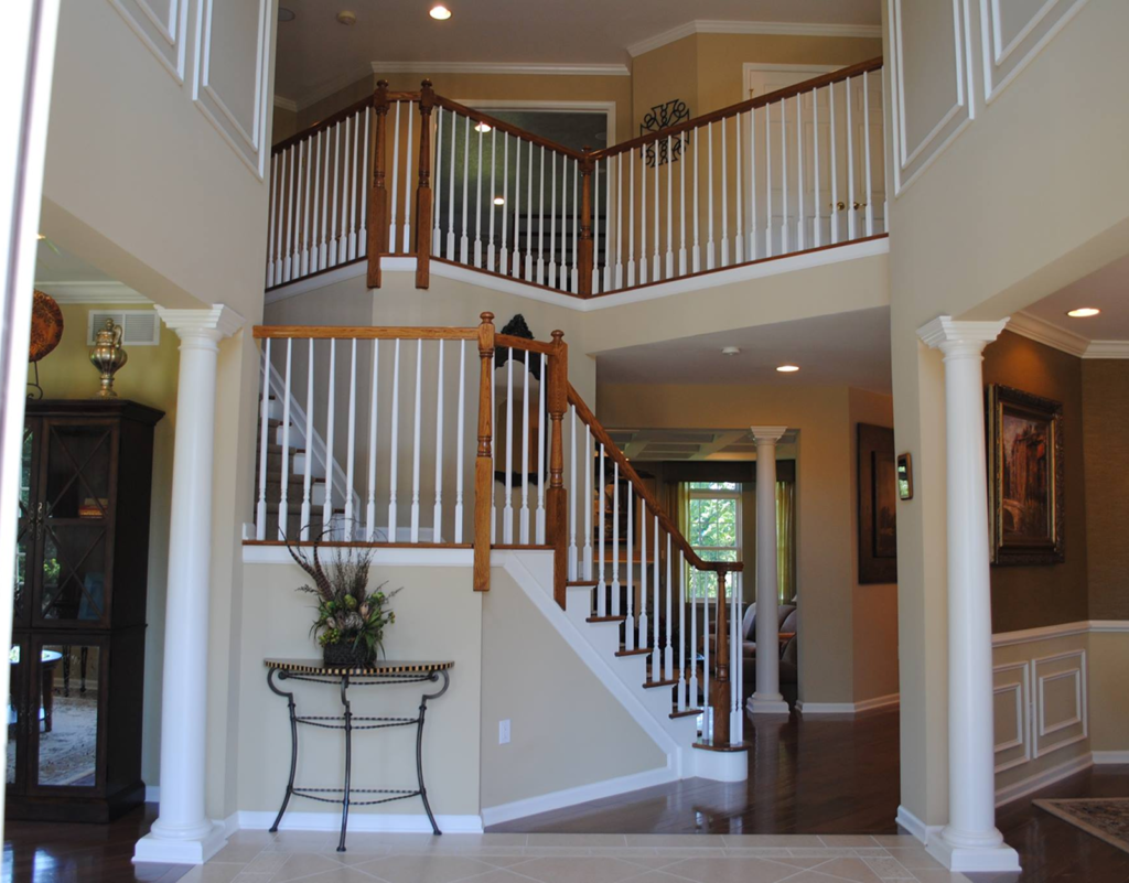 Elegant foyer with wooden staircase, white railings, decorative columns, and a console table adorned with plants, showcasing quality craftsmanship and attention to detail in home interior design.